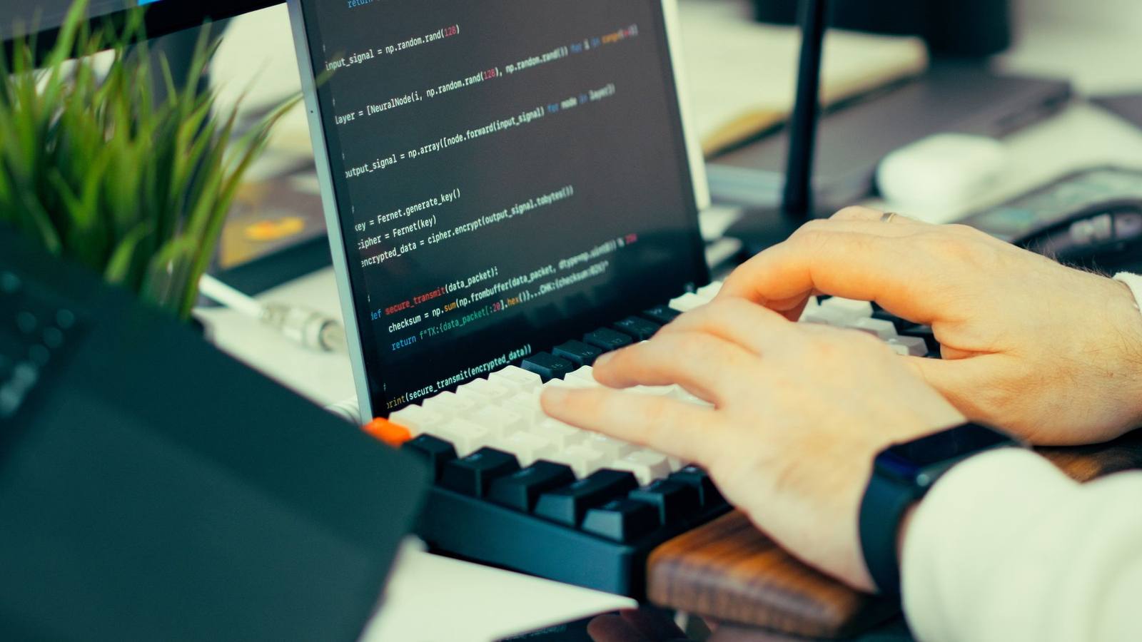 A developer typing on a keyboard in front of a screen showing source code.
