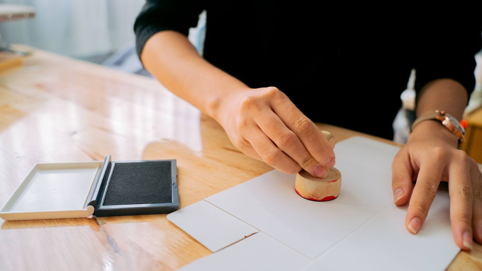 A hand pressing a rubber stamp onto a document on a wooden desk.