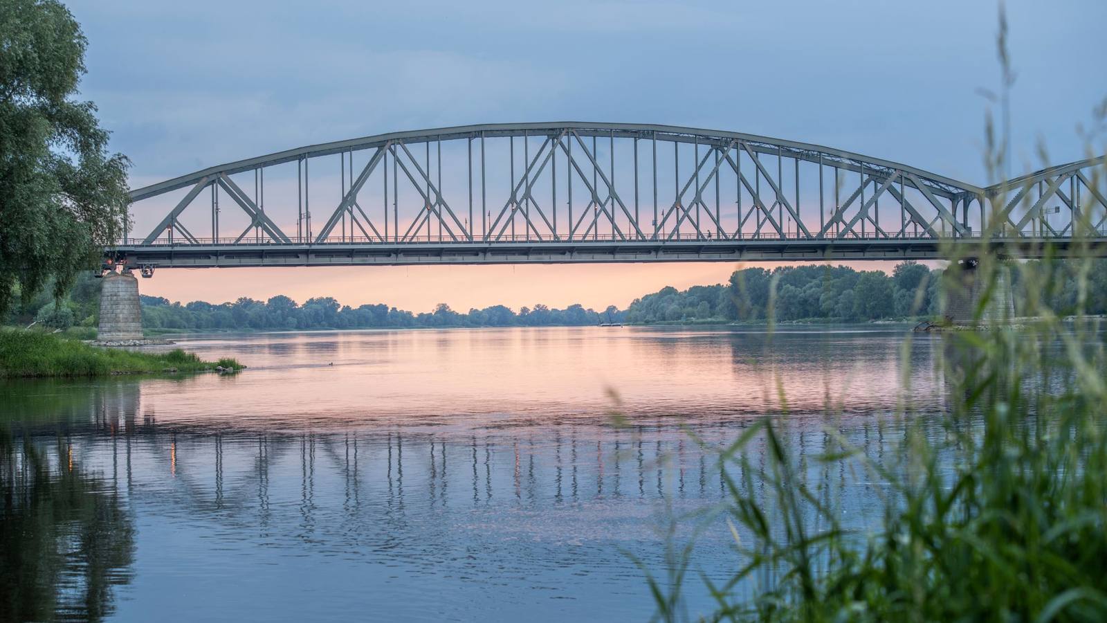 A railway bridge stretching across a calm river at sunset.